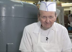 Jim Balmain smiling in front of bakery equipment during his interview at Smith's Bakery in Bakersfield, CA.